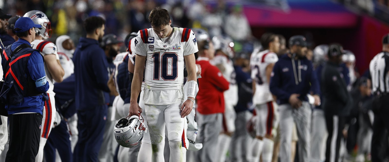 Drake Maye, con el casco en la mano y la cabeza gacha, camina por la banda de los Patriots durante la Super Bowl LX