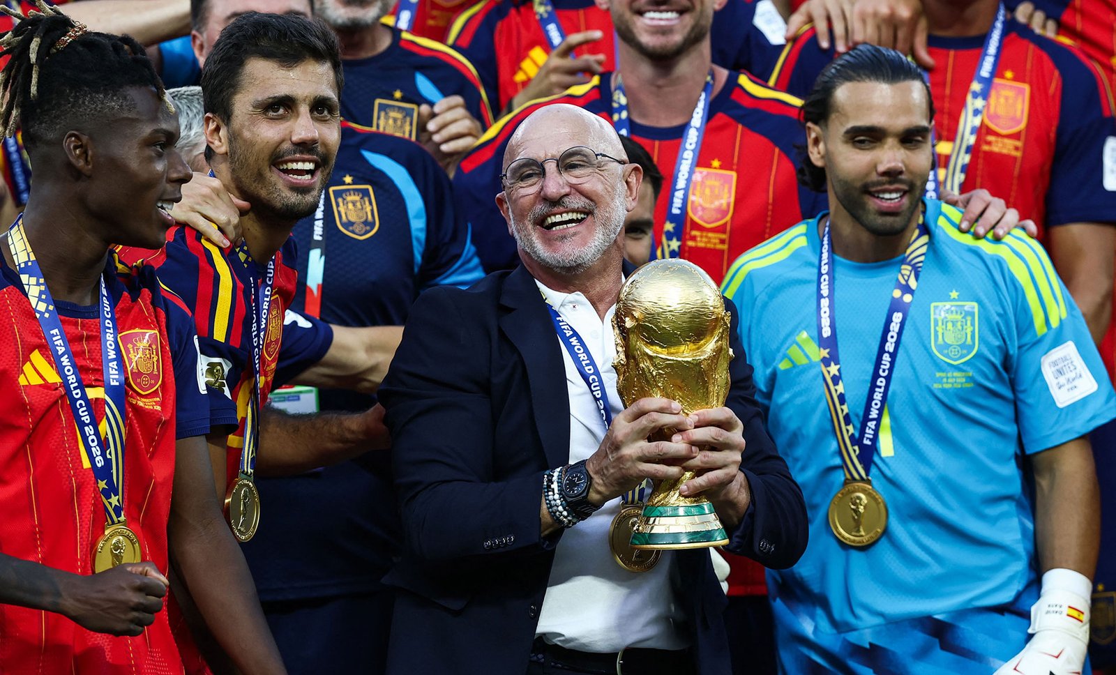 Luis de la Fuente sonríe sosteniendo la Copa del Mundo rodeado de jugadores de España con las medallas de campeón