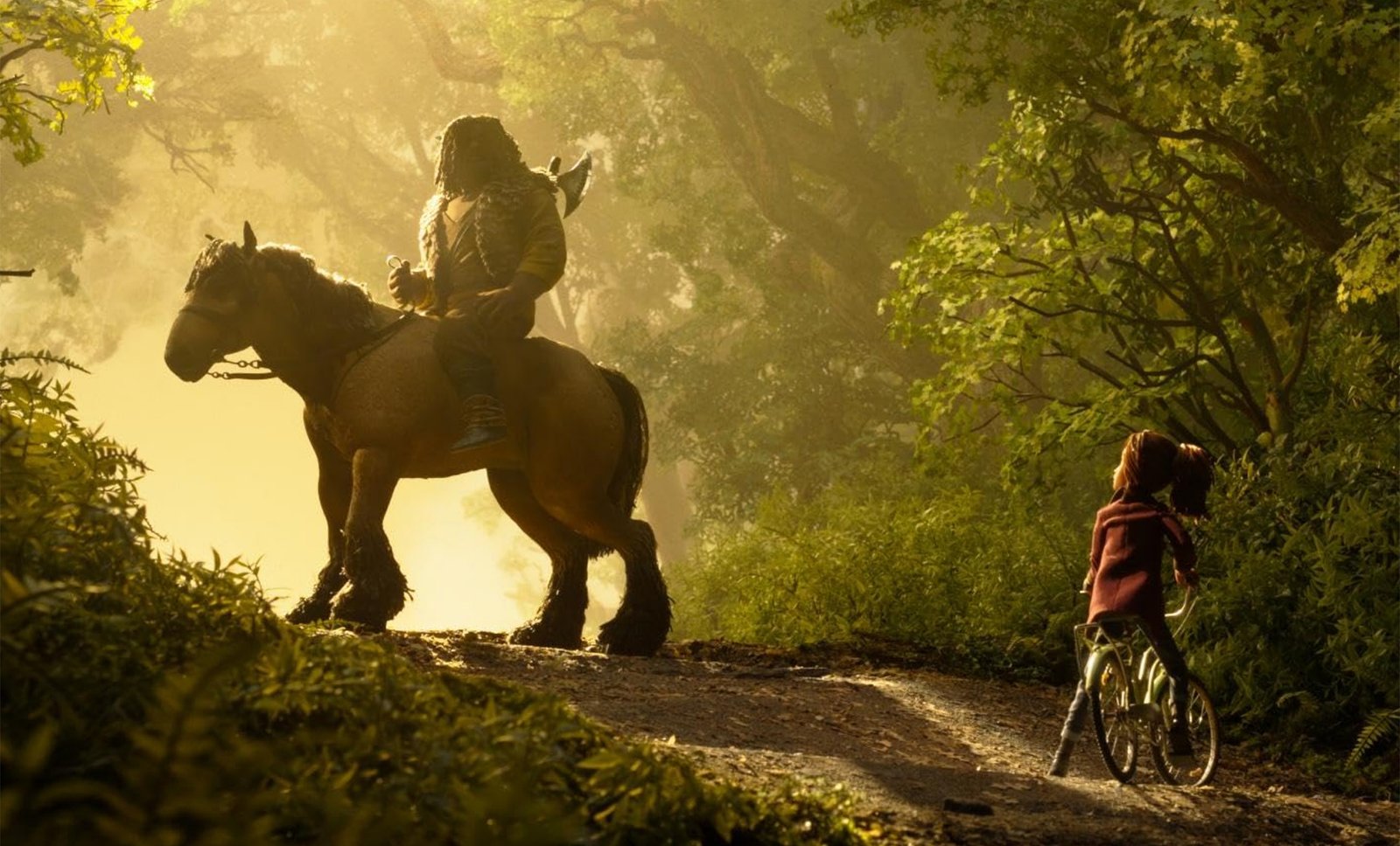 Un guerrero con hacha a lomos de un caballo robusto domina un camino de bosque dorado por la bruma, mientras una niña en bicicleta lo mira desde abajo.